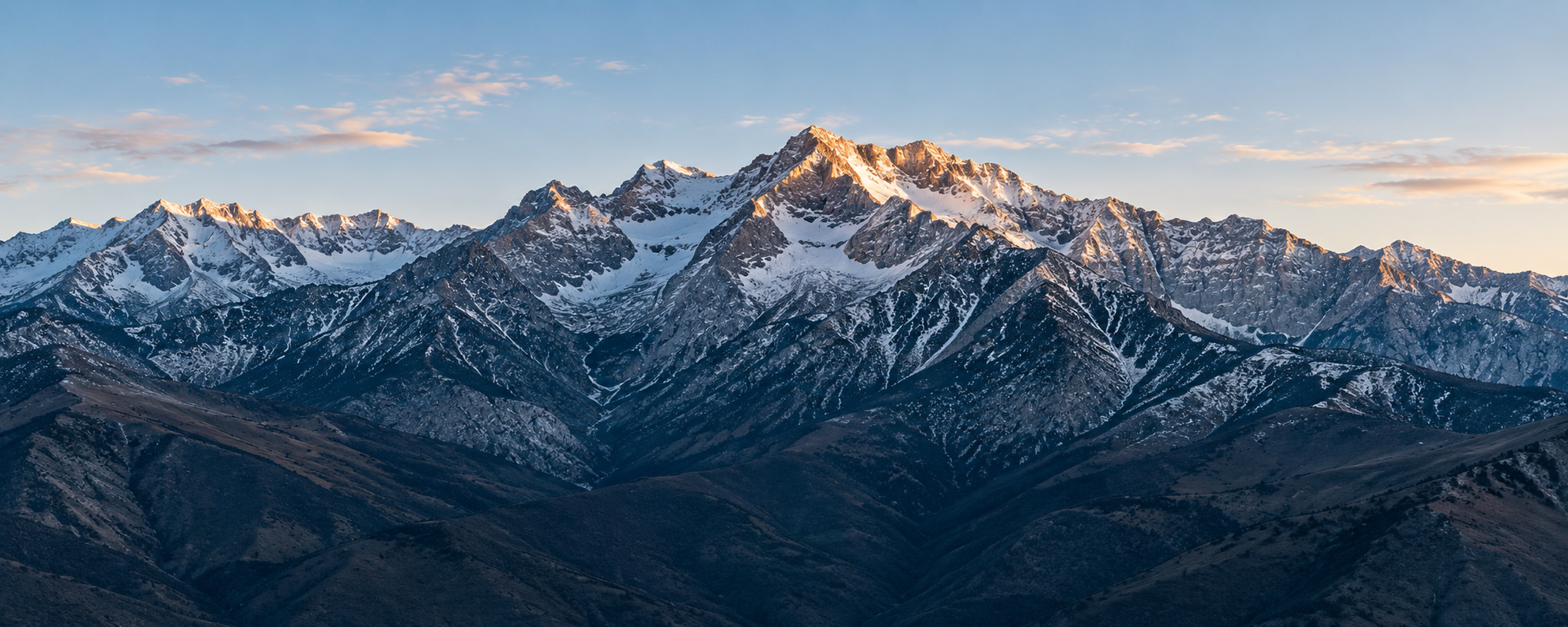 A mountain panorama with snow-covered peaks in soft morning light.